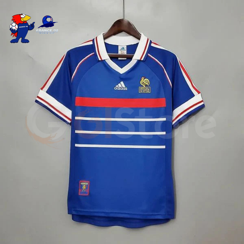 Features a blue body, red and white horizontal chest stripes, a white fold-over collar and tricolor sleeve detailing.
