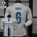 Front and back views of a white Manchester City long-sleeve jersey with blue central stripes, blue Guéhi number 6 print and Etihad Airways sponsor, alongside UCL graphics.