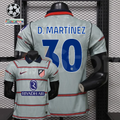 Front and back views of a light grey Atlético Madrid short-sleeve jersey with red horizontal stripes, blue D. Martínez number 30 print and Riyadh Air sponsor, alongside UCL graphics.
