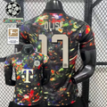  Front and back views of a black Bayern Munich short-sleeve jersey with a multicolored abstract design, cream Olise number 17 print and Telekom sponsor, alongside UCL and Bundesliga graphics.