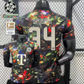 Front and back views of a black Bayern Munich short-sleeve jersey with a multicolored abstract design, cream Saibari number 34 print and Telekom sponsor, alongside UCL and Bundesliga graphics.
