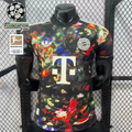 Front view of a black Bayern Munich short-sleeve jersey with a multicolored abstract print, cream club crest, adidas Trefoil and Telekom sponsor, alongside UCL and Bundesliga graphics.