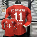 Front and back views of a red Bayern Munich long-sleeve home jersey with tonal stripes, white Brown number 11 print and Telekom sponsor, alongside UCL and Bundesliga badge graphics.