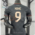 Back view of a dark grey Bayern Munich 2025–2026 short-sleeve third jersey with gold-coloured KANE number 9 printing and red and green collar and cuff trim.