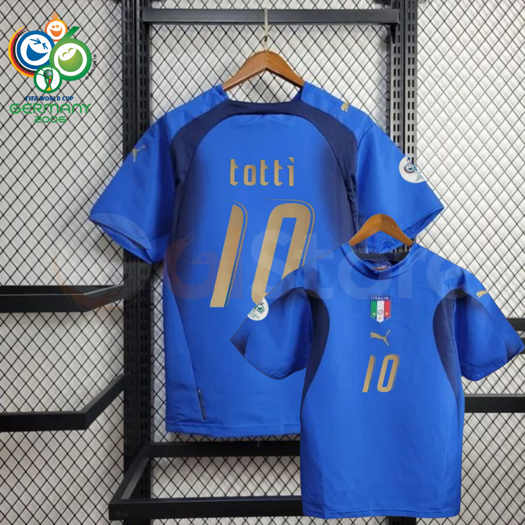 Front and back views of a blue Italy short-sleeve retro home jersey with dark panels, gold Totti number 10 print and sleeve patches, alongside a Germany 2006 World Cup graphic.