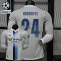 Front and back views of a white Manchester City long-sleeve jersey with blue central stripes, blue Gvardiol number 24 print and Etihad Airways sponsor, alongside UCL graphics.