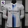 Front view of a white Manchester City long-sleeve jersey with blue central stripes, club crest, Puma logo and Etihad Airways sponsor, alongside Premier League and UCL graphics.