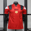 Front view of a red Manchester United short-sleeve jersey with tonal vertical stripes, black and white shoulder panels, a central club crest and black adidas logo.