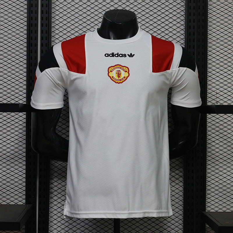 Front view of a white Manchester United short-sleeve jersey with red and black shoulder panels, a central club crest and black adidas trefoil logo.