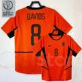 Netherlands orange short-sleeve retro jersey, front and back views with DAVIDS 8 print, black collar and side panels, alongside a 2002 World Cup graphic.
