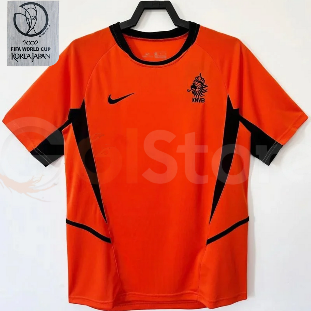 Netherlands orange short-sleeve retro jersey with black collar, black side panels and KNVB lion crest, alongside a 2002 World Cup patch graphic.
