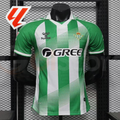 Real Betis green and white striped short-sleeve jersey with diagonal line details, a white collar, club crest and GREE sponsor, alongside a red LaLiga graphic.
