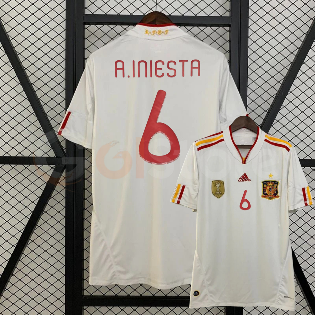 Spain white short-sleeve retro jersey shown from the front and back, with red A. INIESTA 6 print, red and yellow shoulder stripes and a gold FIFA World Champions chest badge.
