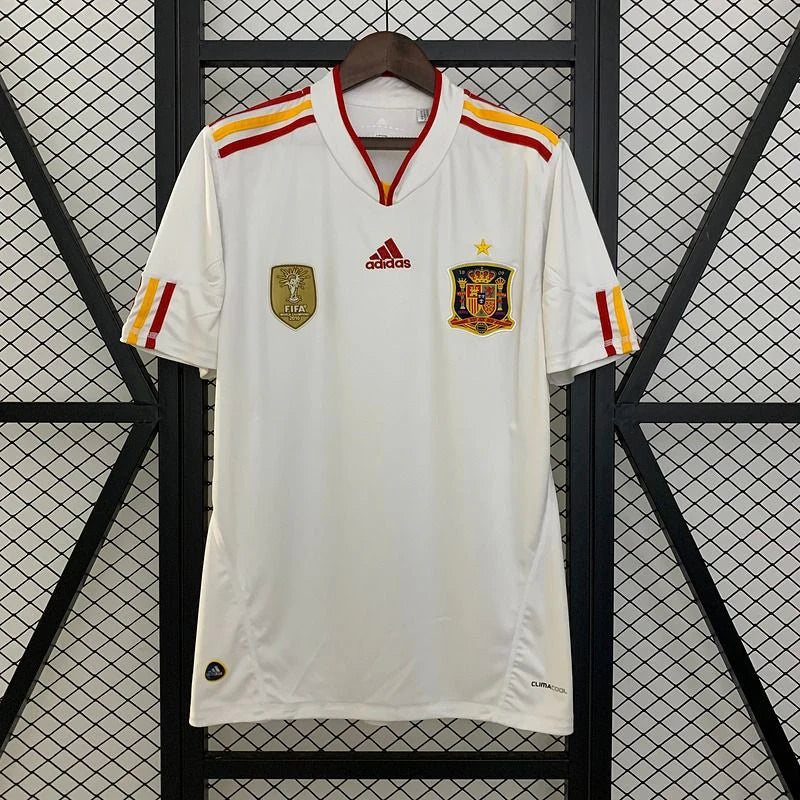 Spain white short-sleeve retro jersey with red and yellow shoulder stripes, a V-neck collar, Spain crest with a gold star and a gold FIFA World Champions chest badge.
