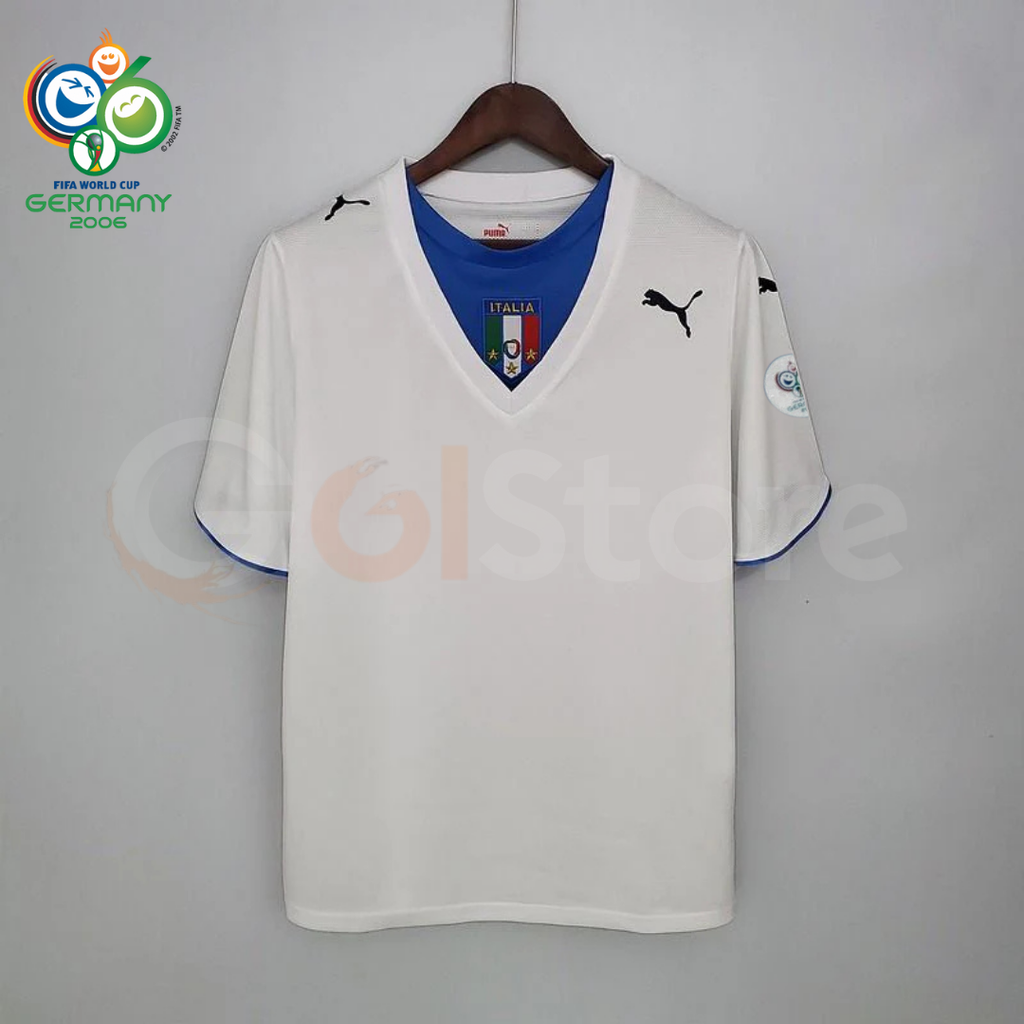 Front view of a white Italy short-sleeve retro away jersey with a blue neckline panel, central Italy crest, black Puma logos and a sleeve patch, alongside a Germany 2006 World Cup graphic.