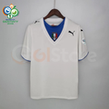 Front view of a white Italy short-sleeve retro away jersey with a blue neckline panel, central Italy crest, black Puma logos and a sleeve patch, alongside a Germany 2006 World Cup graphic.