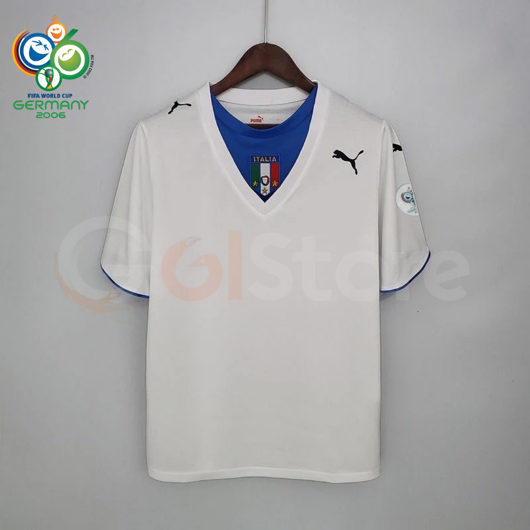 Front view of a white Italy short-sleeve retro away jersey with a blue neckline panel, central Italy crest, black Puma logos and a sleeve patch, alongside a Germany 2006 World Cup graphic.